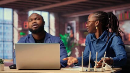 Discouraged African American couple struggles with an unstable Wi Fi network, getting angry while they are troubleshooting to fix the error. Stressed people with lots of remote tasks. Camera B.