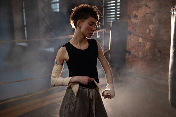 A woman in a boxing ring, wrapping an elastic bandage around her arms, preparing for boxing training. The photo is in a cinematic style, the light gives the mood to a sports motivational story about