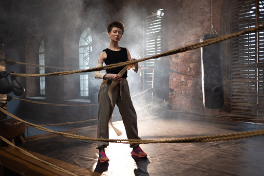 A woman in a boxing ring, wrapping an elastic bandage around her arms, preparing for boxing training. The photo is in a cinematic style, the light gives the mood to a sports motivational story about