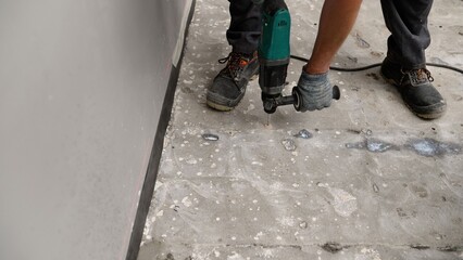 Construction worker removing deteriorating concrete with high-powered rotary hammer drill, demonstrating precision and physical effort during industrial renovation process