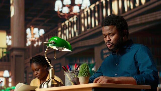 Black university student highlighting relevant phrases to learn the summary of the class lesson, memorizing key information by underlining important terms. Academic library. Camera B.