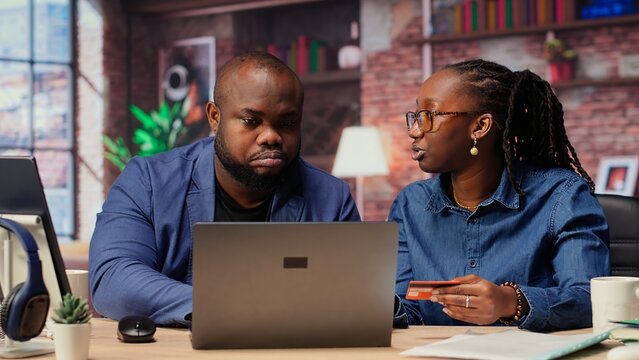 Young people using a card to check the financial balance before buying or paying something, e commerce from the home office. African american couple doing web transactions. Camera B. - Powered by Adobe