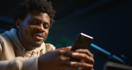 African american young adult enjoying a break from remote work and texting, having fun on social media apps with his friends. Freelancer relaxing and scrolling websites on phone. Camera B.