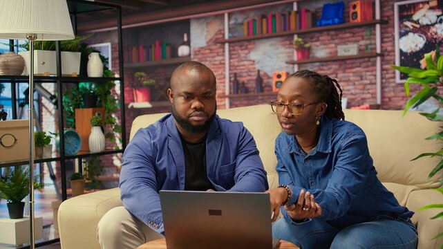African american couple work on a management project for freelancing, using a laptop to research business trends and manage an online brand. Successful remote career development. Camera A.