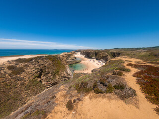 Stunning view of Porto Covinho beach with golden cliffs, calm turquoise waters, and clear blue sky on a sunny day in Portugal&rsquo;s scenic Alentejo coast.