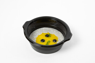 yellow pudding and chia seeds in a plate, sprinkled with berries and mint on a white background