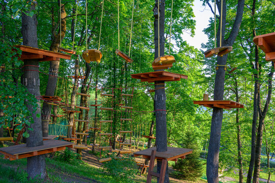 Adventure park with wooden rope bridges and platforms in lush green forest. Outdoor fun and active recreation in treetop rope course with climbing structures on trees in summer day.