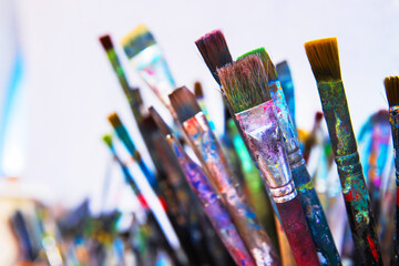 A cluster of well used paintbrushes with colorful dried paint on their handles and bristles in container in creative art studio.