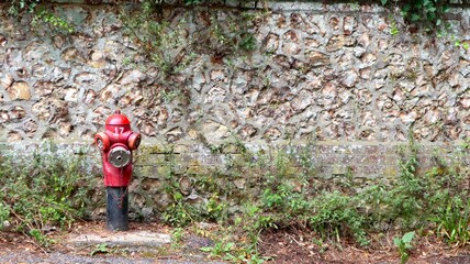 French fire hydrant in front of a stone wall in Normandy, France. Red and iconic.