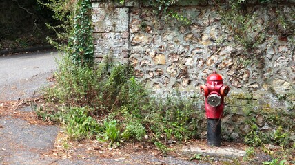 French fire hydrant in front of a stone wall in Normandy, France. Red and iconic.