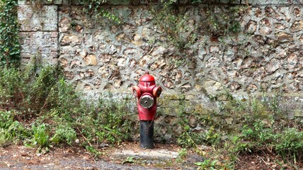 French fire hydrant in front of a stone wall in Normandy, France. Red and iconic.