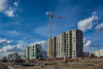 Blurred image captures the essence of a construction site, featuring multiple buildings and a towering crane under a vast sky.