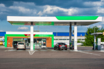 Fototapeta premium Blurred image of a modern gas station with cars and vans refueling. Urban background with residential buildings. Concepts of transport, travel and urban infrastructure.