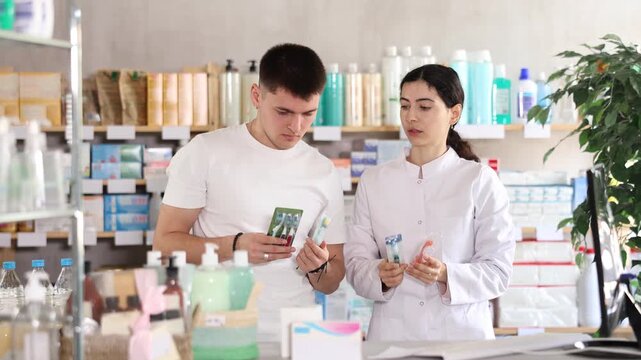 Guy chooses toothbrush in modern pharmacy. Female pharmacist helps with choosing . High quality 4k footage