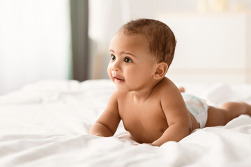 Closeup portrait of sweet naked black baby crawling on bed on the white bedsheets, indoors. Cute...