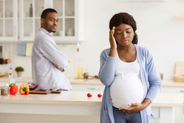 Pregnant black woman having quarrel with husband while cooking together in kitchen, copy space....