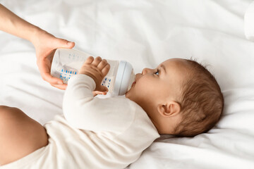 Nursery And Childcare Concept. Portrait of cute little black kid drinking milk, babysitter holding...