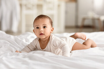 Cute Smiling African Baby Lying On Stomach Looking Away In Bedroom At Home. Toddler Kid Crawling On...