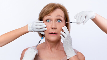 Shocked mature lady receiving beauty shots, using injection medicine to prevent aging on light...