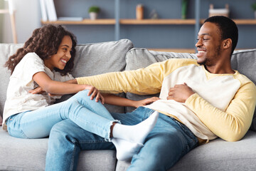 Loving black father and daughter tickling each other while resting on sofa in cozy living room, copy space. Happy african american family school girl kid and dad spending time together