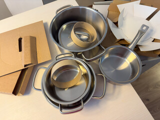 18/8 Stainless steel pots and a frying pan are freshly unpacked and placed on a kitchen table, surrounded by cardboard packaging. Flat lay, ugc