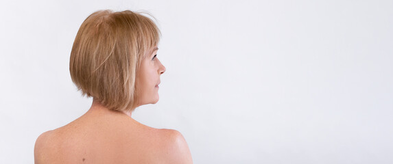 Back view of beautiful senior lady posing half-naked over white studio background, looking at copy...
