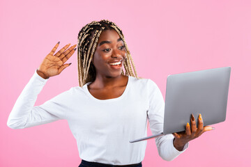 Cheerful African American woman waving on laptop screen, have video call on pink studio background