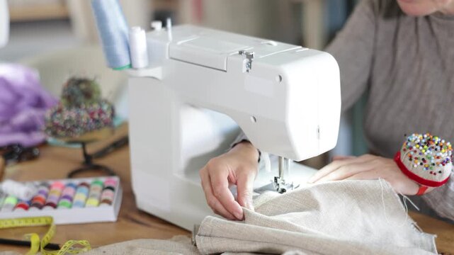 Close-up of professional female seamstress hands working at sewing machine, stitching checkered fabric with focus and precision at table in workshop. High quality 4k footage