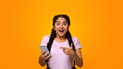 Yes, Great News. Portrait Of Excited Indian Woman Celebrating Win, Using Smartphone And Pointing At...