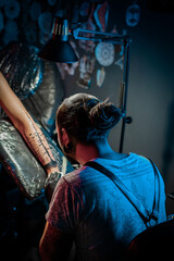 Man tattoo master with dreadlocks showing process creation tattoo, female body 