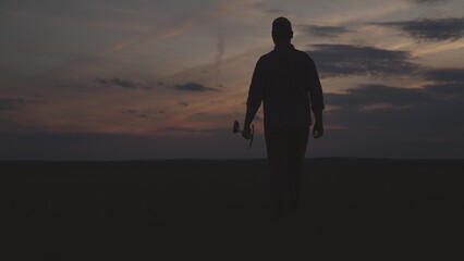 farming, silhouette of man walks with shovel in his hands across field against background of sunset...