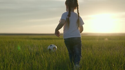 Little child plays soccer with soccer ball on the green field of the stadium at sunset,...