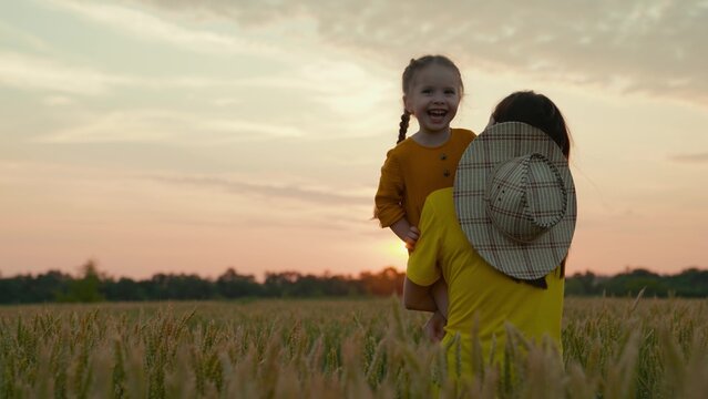 A kind farmer mother with a child in a field with wheat at sunset, growing grain for making bread, a happy child, a family business on a ranch, examining the grown crops with a baby in her arms.