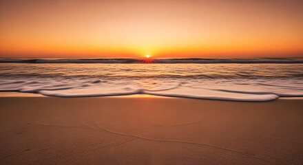 Obraz premium The sun rises over the ocean, illuminating the sandy beach with golden light