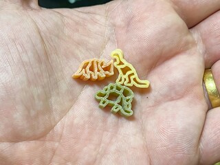 Colorful dinosaur-shaped pasta in the open hand.