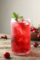 Tasty cherry soda with ice cubes, berries and mint on wooden table, closeup