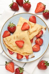 Delicious crepes with strawberries and cream on white wooden table, flat lay