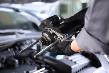Auto part. Professional mechanic with starter motor near open hood of car indoors, closeup