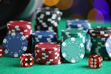 Casino chips and dice on green table against blurred lights, closeup