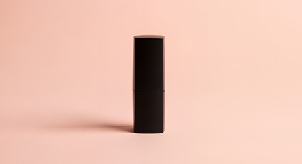 A sleek black lipstick tube stands upright against a soft, pale pink background, showcasing its simple elegance and minimalist design.