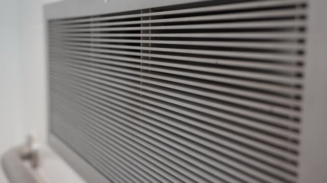 Detailed close-up of a metal ventilation grille indoors. Part of an air conditioning or ventilation system mounted on the wall.