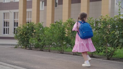 little cheerful girl runs school with backpack on her shoulders, happy kid is in hurry to first lesson, baby will receive primary preschool education, child will gain new knowledge in the classroom.