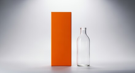 A tall, slender, clear glass bottle stands next to a vibrant orange rectangular box on a light gray , creating a simple yet elegant product display.