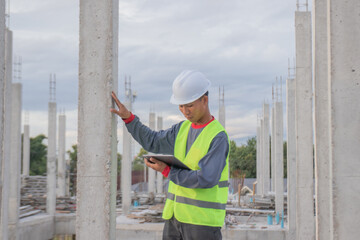 Confident young male engineer wearing hard hat, checking checklist and blueprints at construction...