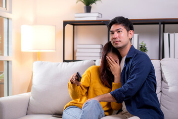 Young asian couple watching a scary or thrilling TV show in living room at home with emotion shock and scared, emotion reaction while watching horror television with fear, lifestyle and bonding.