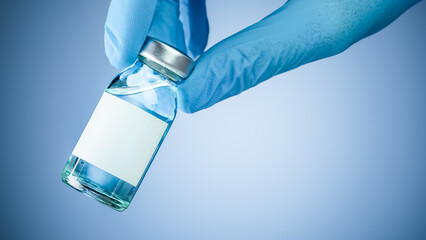 Nurses hand in blue medical gloves holding a medical vaccine vial with blank white copy space for text. Healthcare concept of prevention, treatment, or new pharmaceutical drugs.