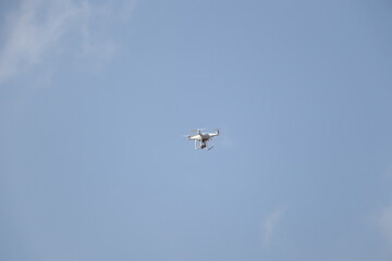 A white unmanned aerial vehicle with a camera flying in the blue sky.