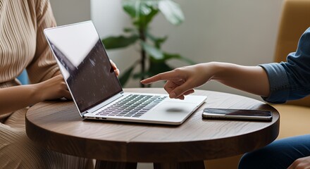 Two colleagues collaborate on a laptop, one pointing at the screen to discuss a project or idea together.