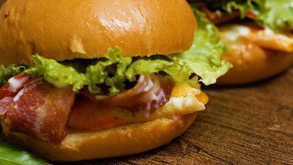Two mouthwatering cheeseburgers featuring crispy bacon, fresh lettuce, ripe tomato, and gooey melted cheese on toasted brioche buns resting on a rustic wooden table