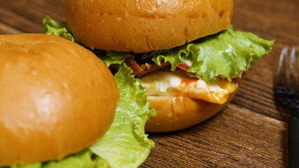 Two appetizing burgers with fresh lettuce, crispy bacon, fried egg, melted cheese, and sauce are placed on a rustic wooden table, ready to be enjoyed